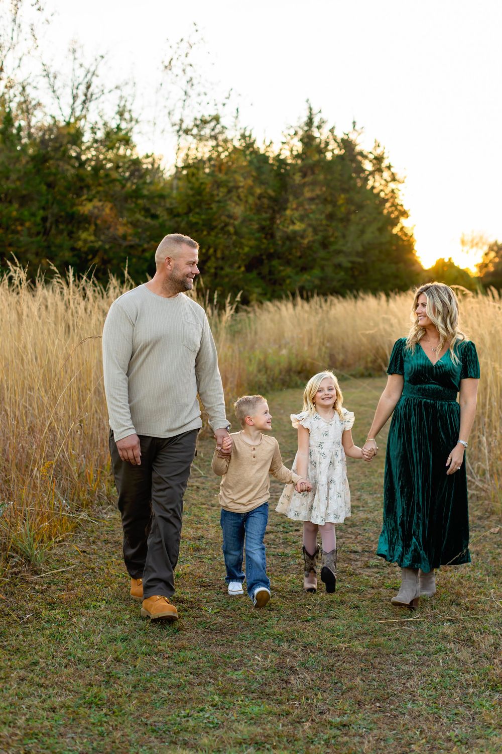 A family walks together through a golden field at sunset while holding hands.
