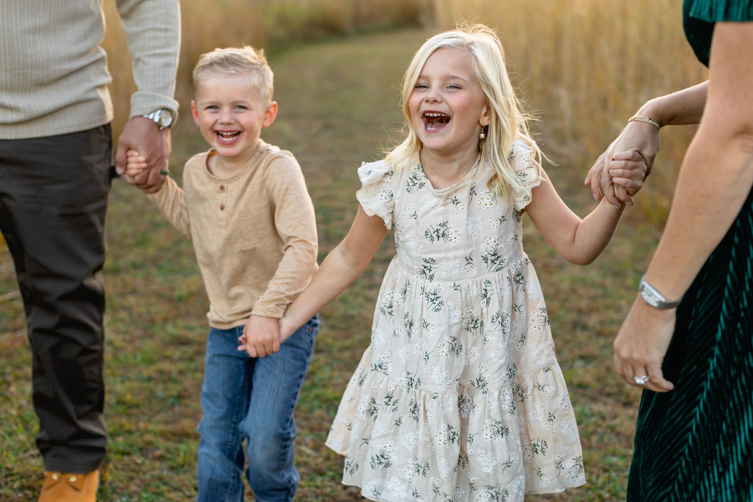 Family walking together and laughing joyfully in a grassy outdoor setting at golden hour.