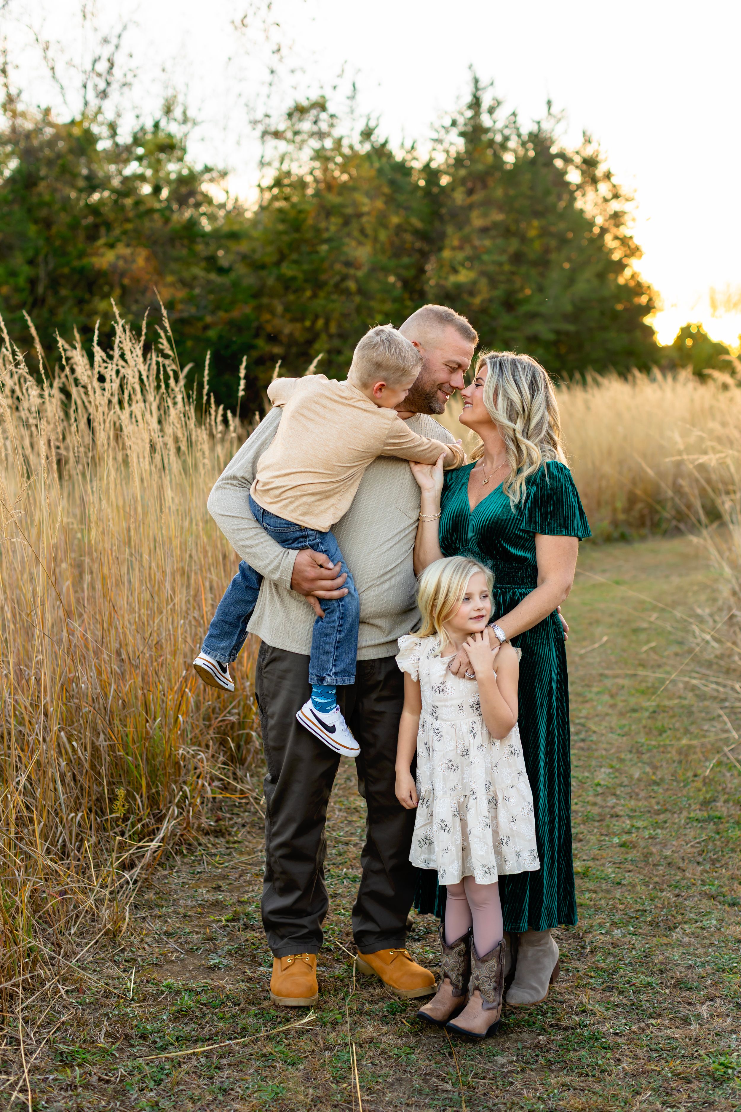 A group embraces while standing in a golden field during sunset with tall grass surrounding them.
