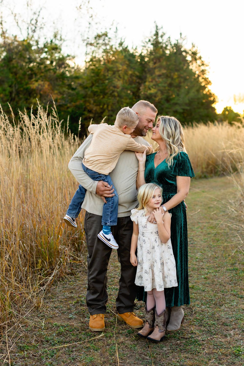 A group embraces while standing in a golden field during sunset with tall grass surrounding them.