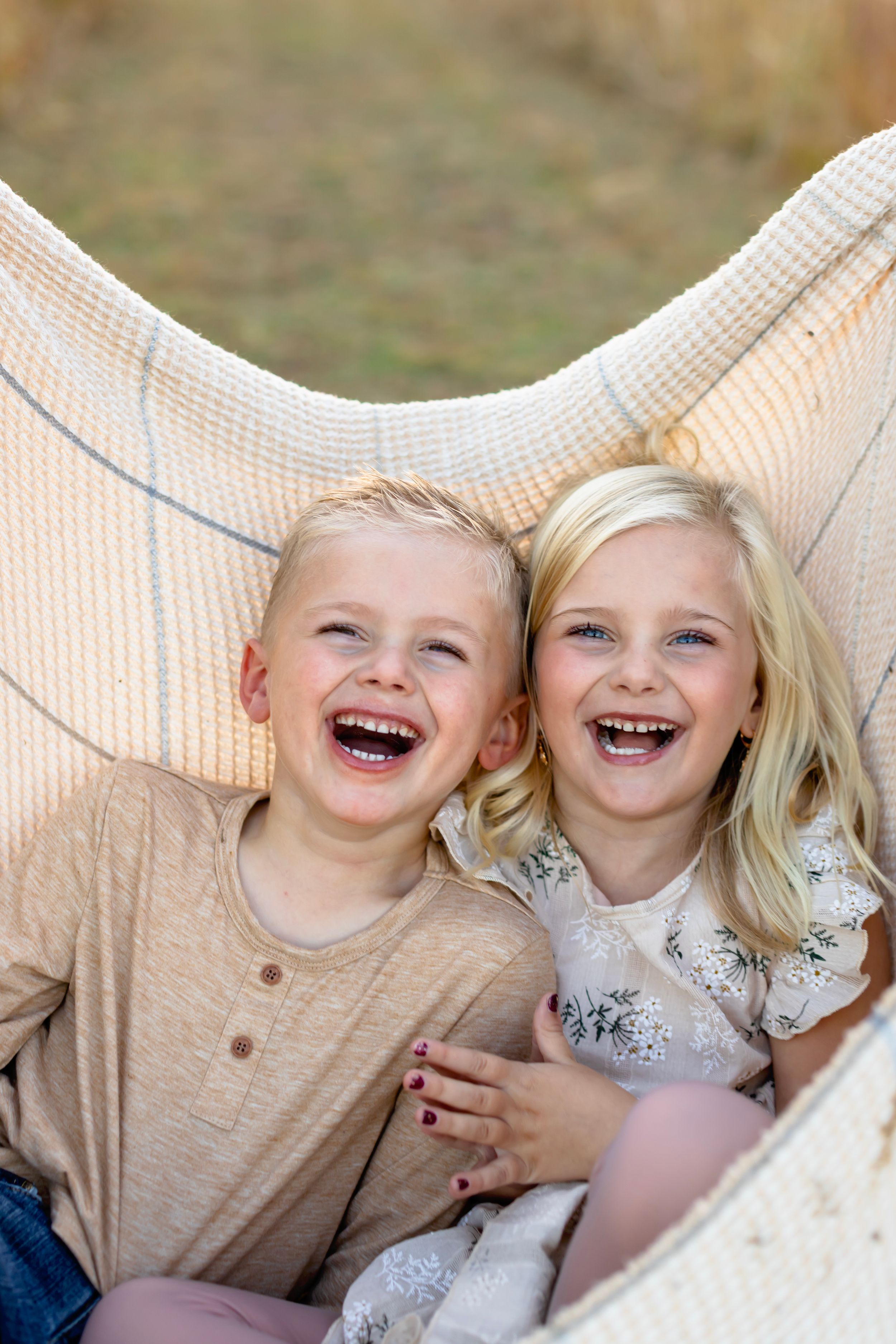 Two children wearing beige and floral outfits laugh joyfully together in a series of candid outdoor photos.