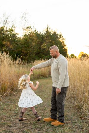A heartwarming dance moment between parent and child in a field of tall grass at sunset.