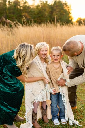 A joyful family moment captured in a golden field at sunset with warm autumn colors and casual coordinated outfits.