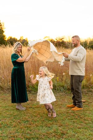 Family plays together in an autumn field with a white blanket during golden hour photography session.