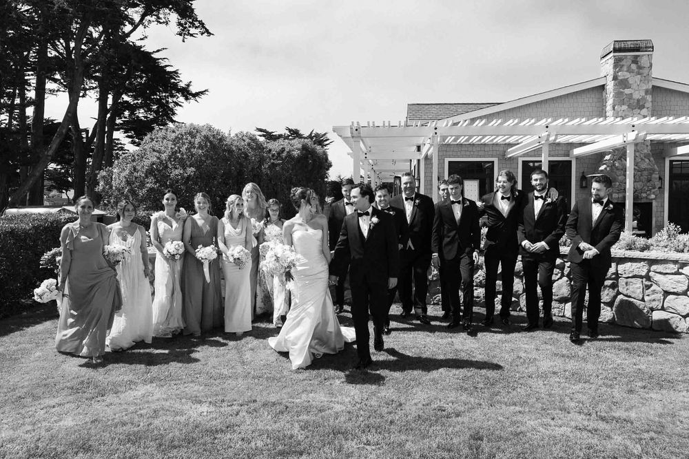 Black and white photo of a wedding party lined up outdoors on a lawn in front of a stone building.