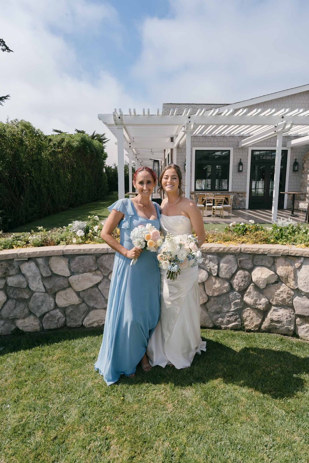 Wedding party members in light blue dresses and white gown pose by a stone wall at an outdoor venue.
