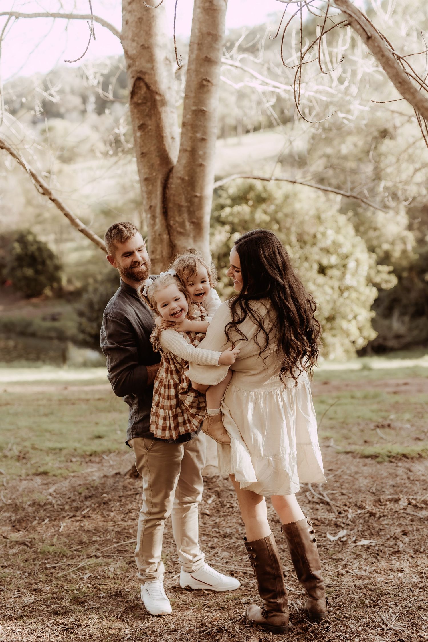 Children playing together under large trees in a natural outdoor setting.