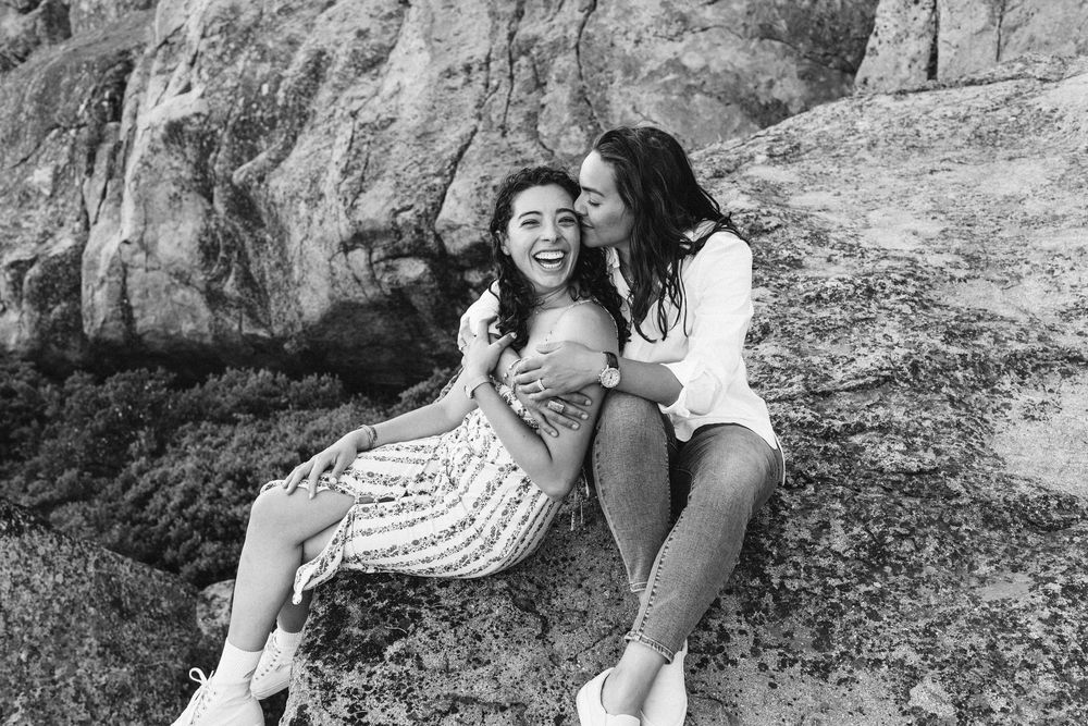 Two friends laughing together while sitting on rocky terrain in black and white.