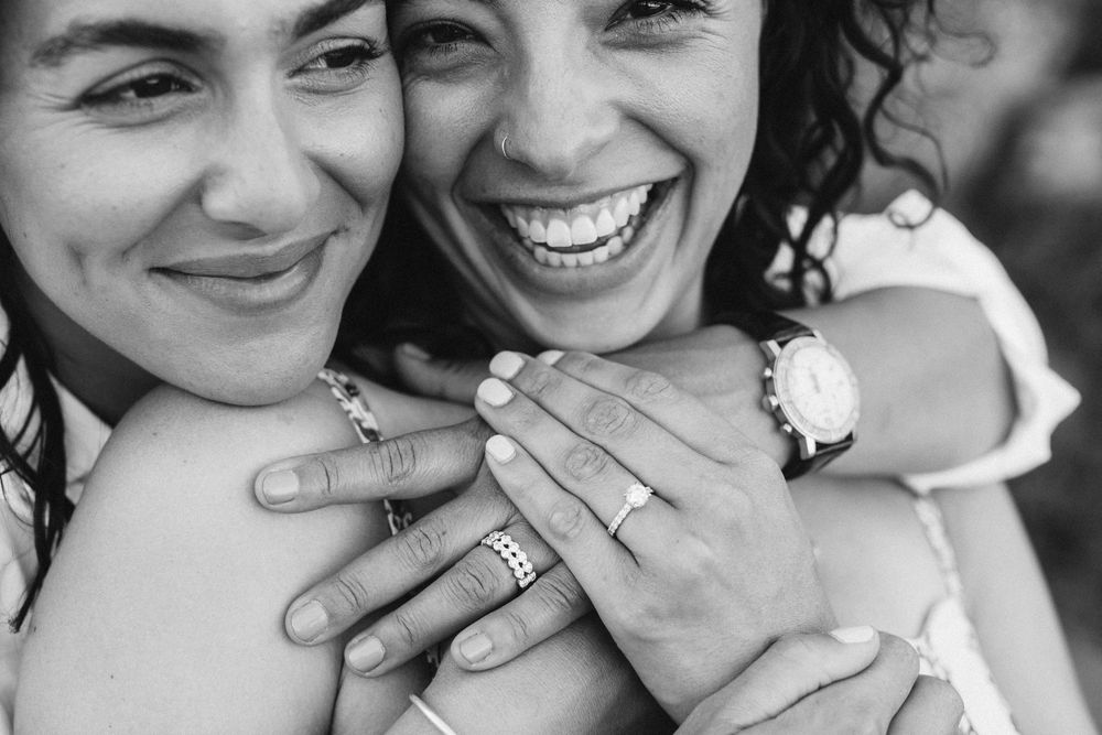 Close-up black and white photo showing hands with rings and joyful expressions.
