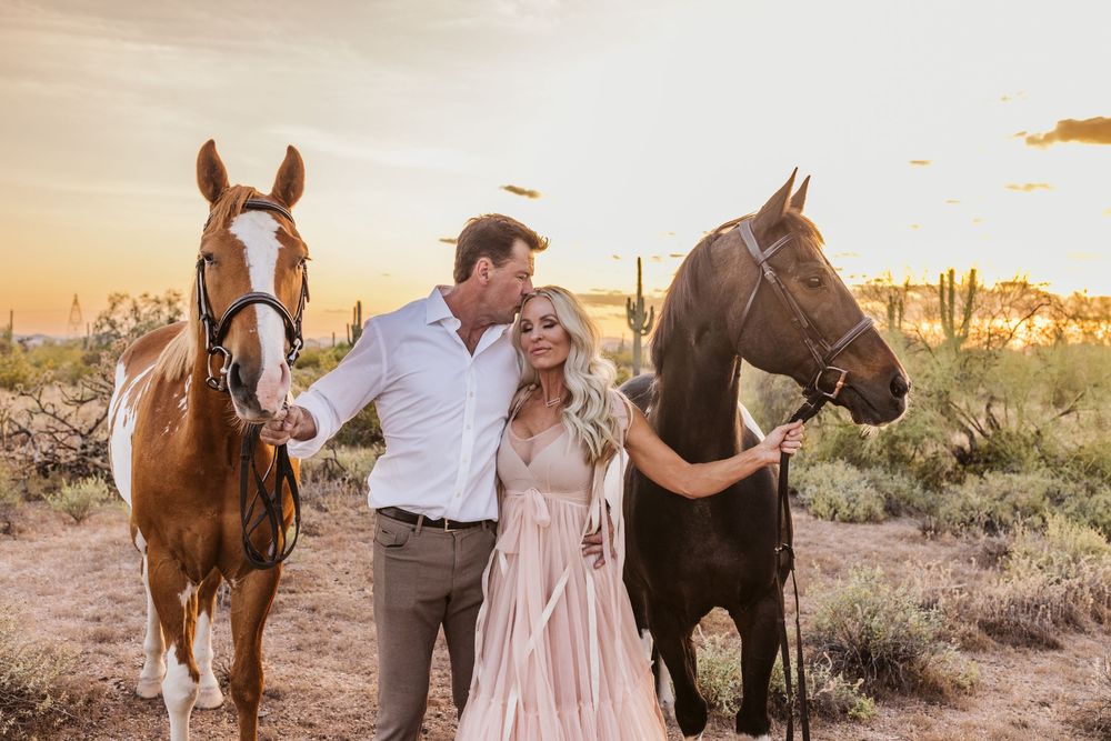 Romantic desert photoshoot with two horses and couple in formal attire at golden hour.