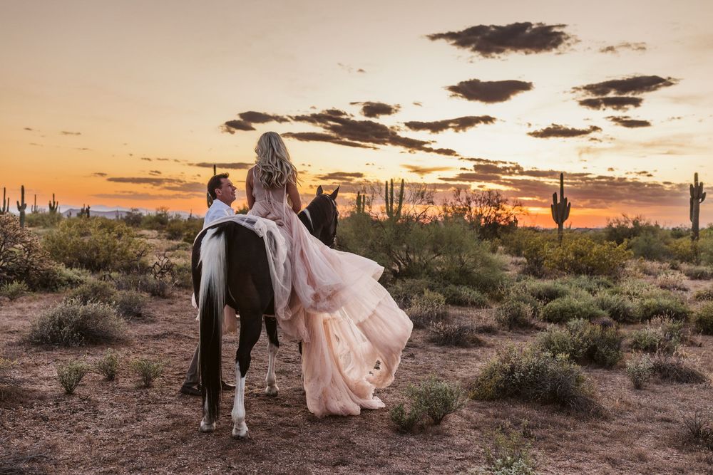 Couple with horses in desert landscape at sunset with saguaro cacti silhouettes.