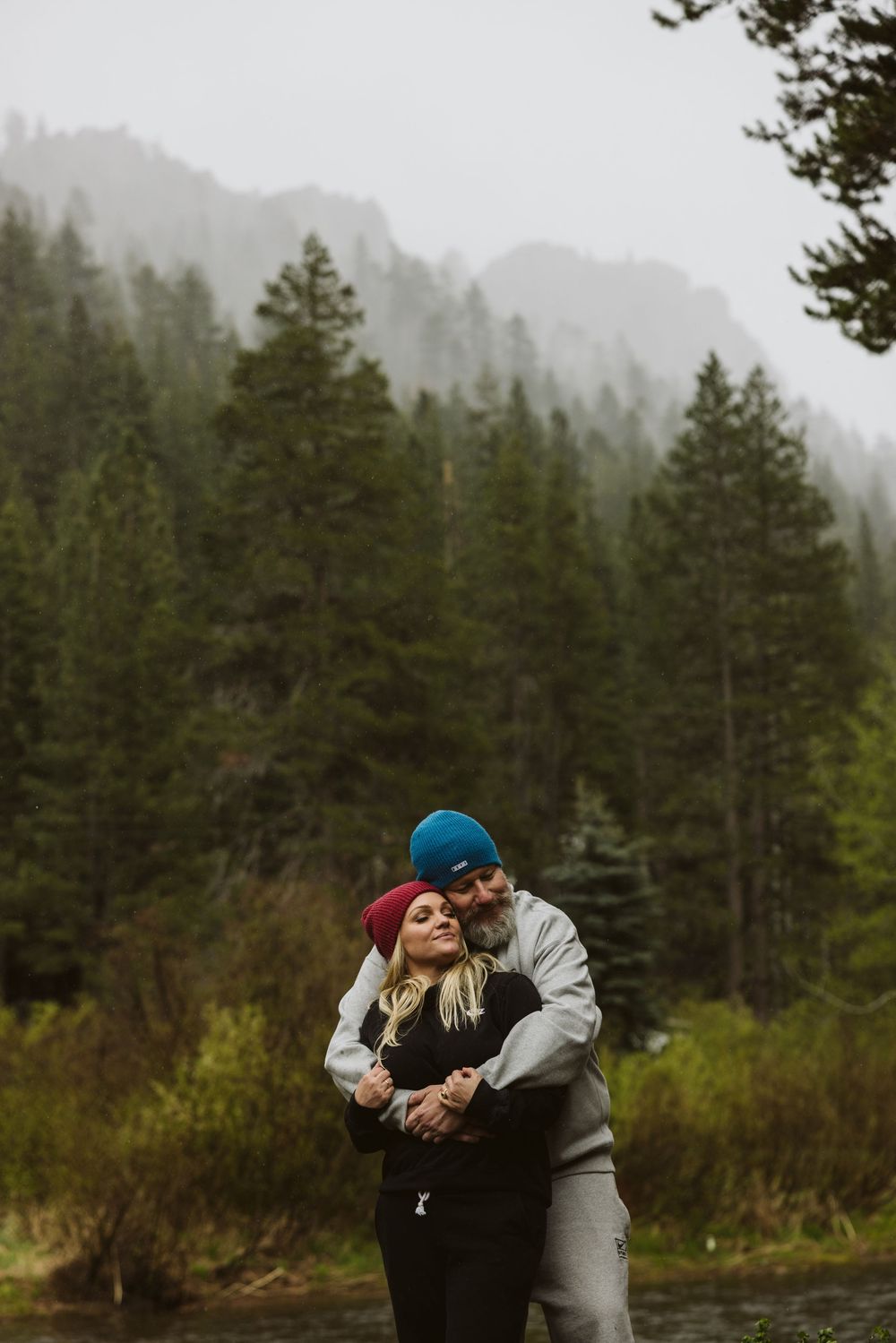 Couple embracing in foggy mountain forest with evergreen trees in background.