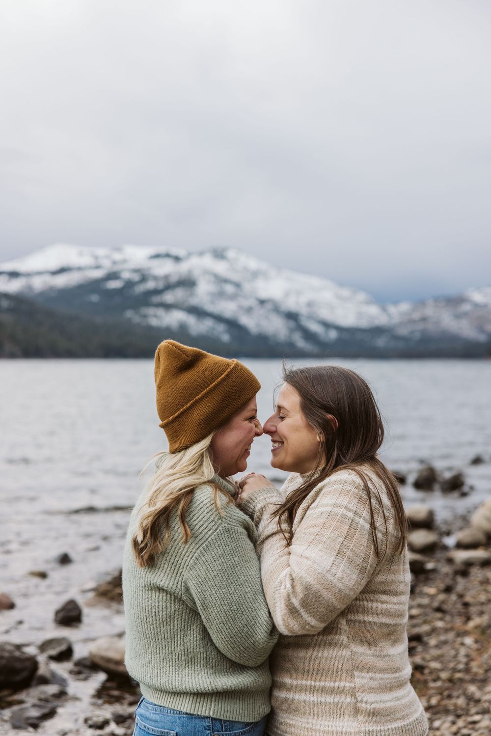 Two people in cozy sweaters sharing a tender moment by a snowy lake.