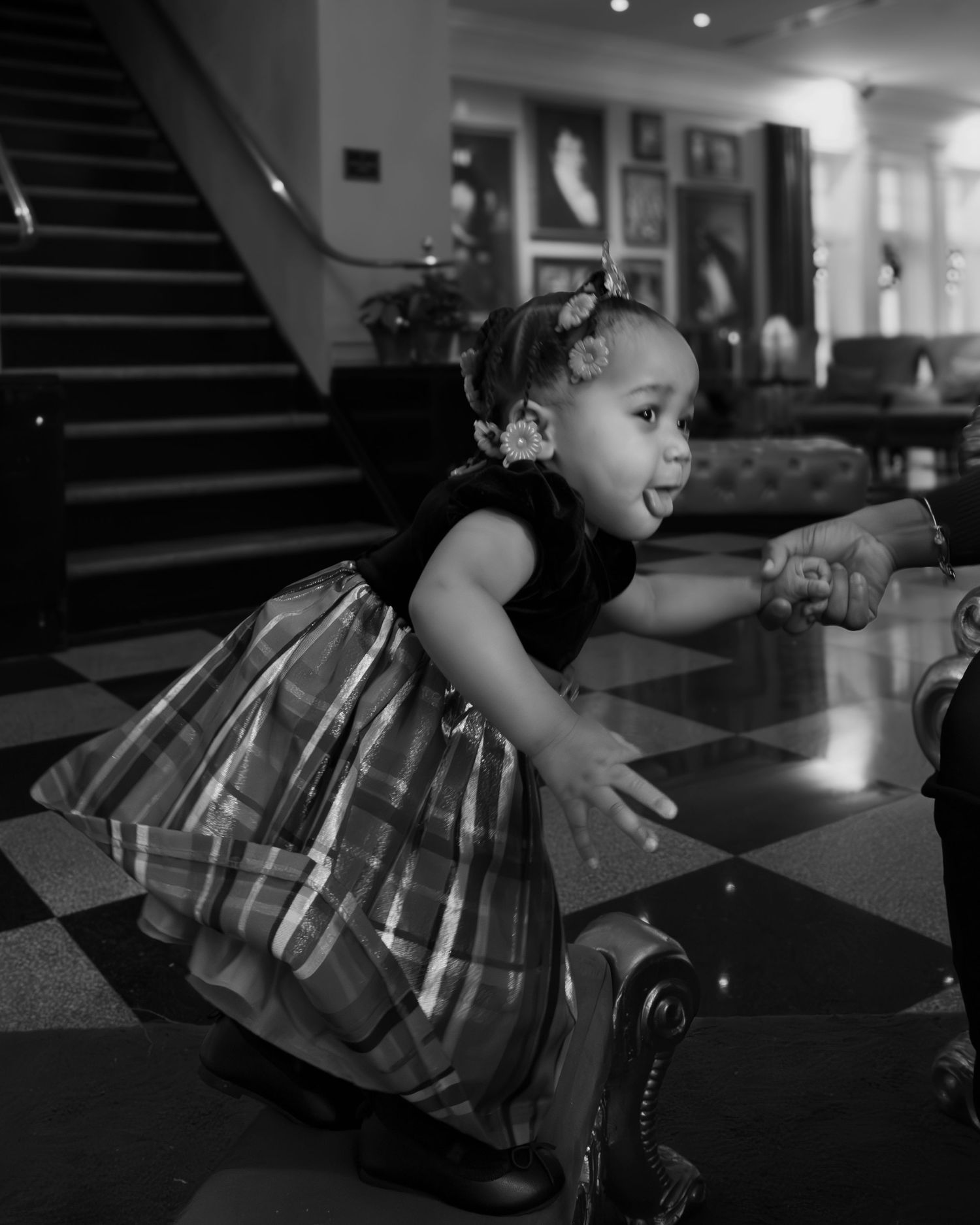 Black and white series showing a small child in a plaid dress playing and crawling on a dark surface.