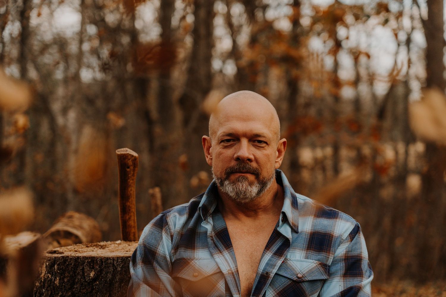 A person wearing a plaid shirt stands in an autumn forest with golden leaves and warm lighting.