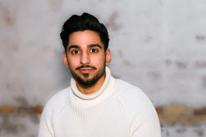 Person in cream sweater against textured background.