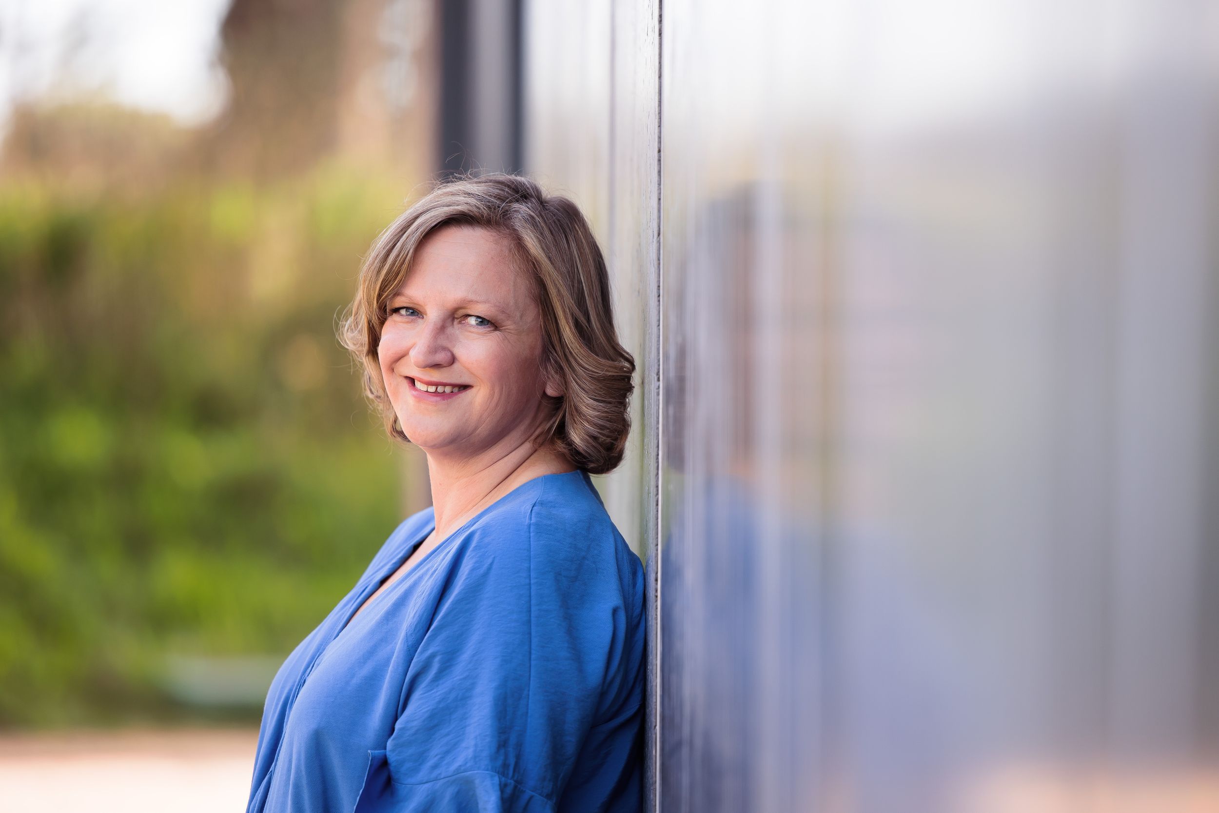 Person in bright blue blazer leaning against wall outdoors.