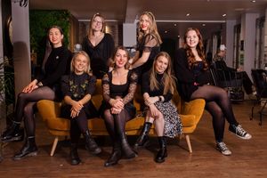 Group of people in black outfits posing together on orange couch.