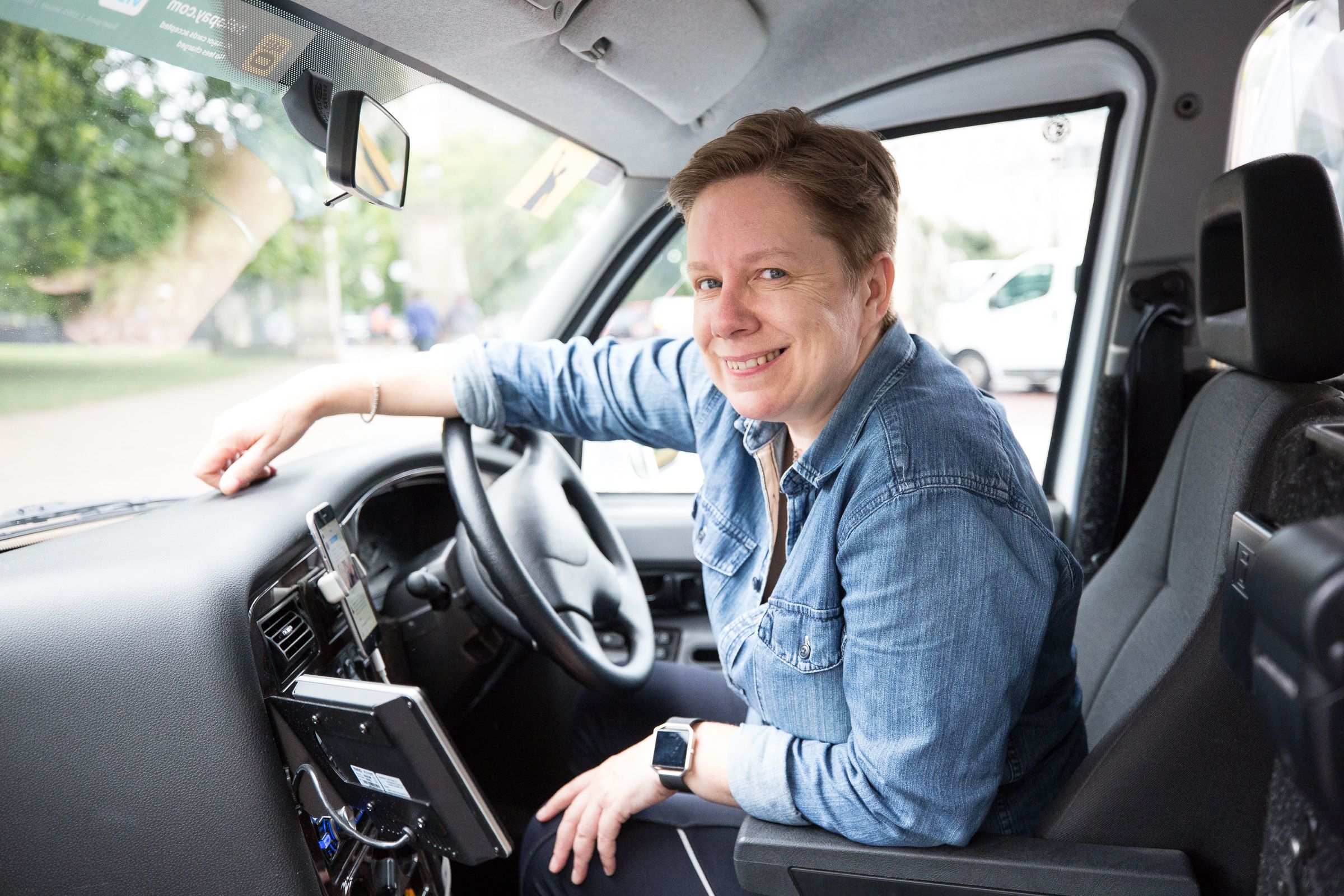 Person sitting in driver's seat of car wearing denim shirt.