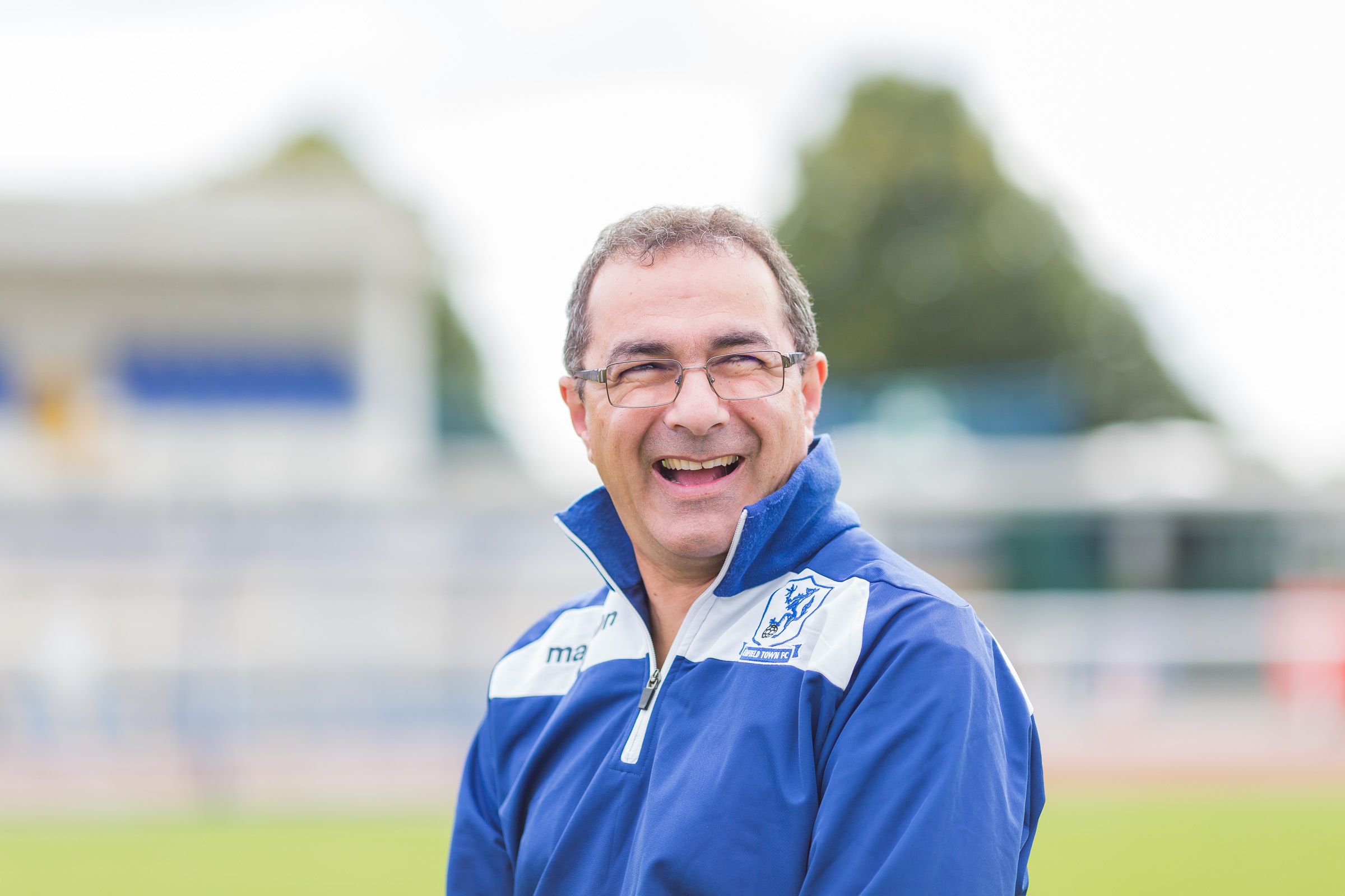 Person in blue athletic jacket smiling outdoors at a sports field.