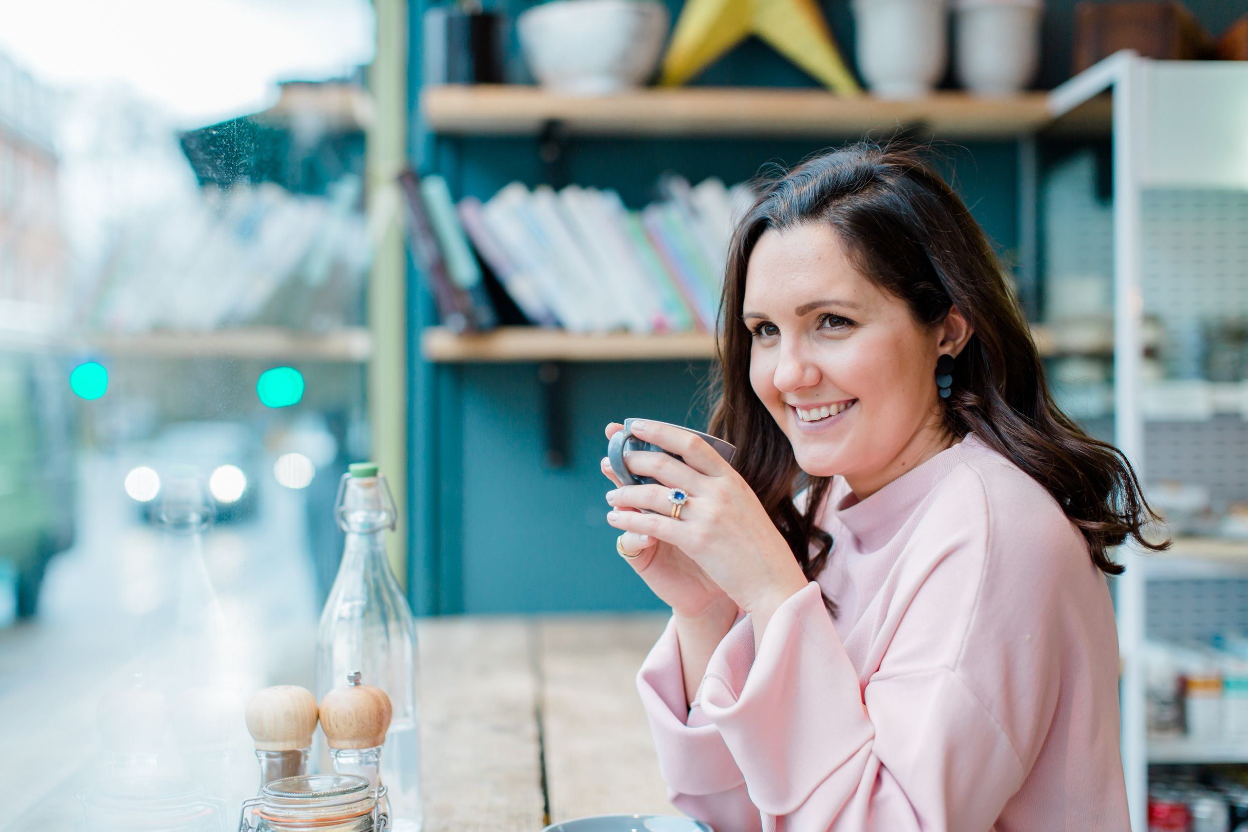 Person enjoying coffee at an outdoor cafe with turquoise shelving in the background.