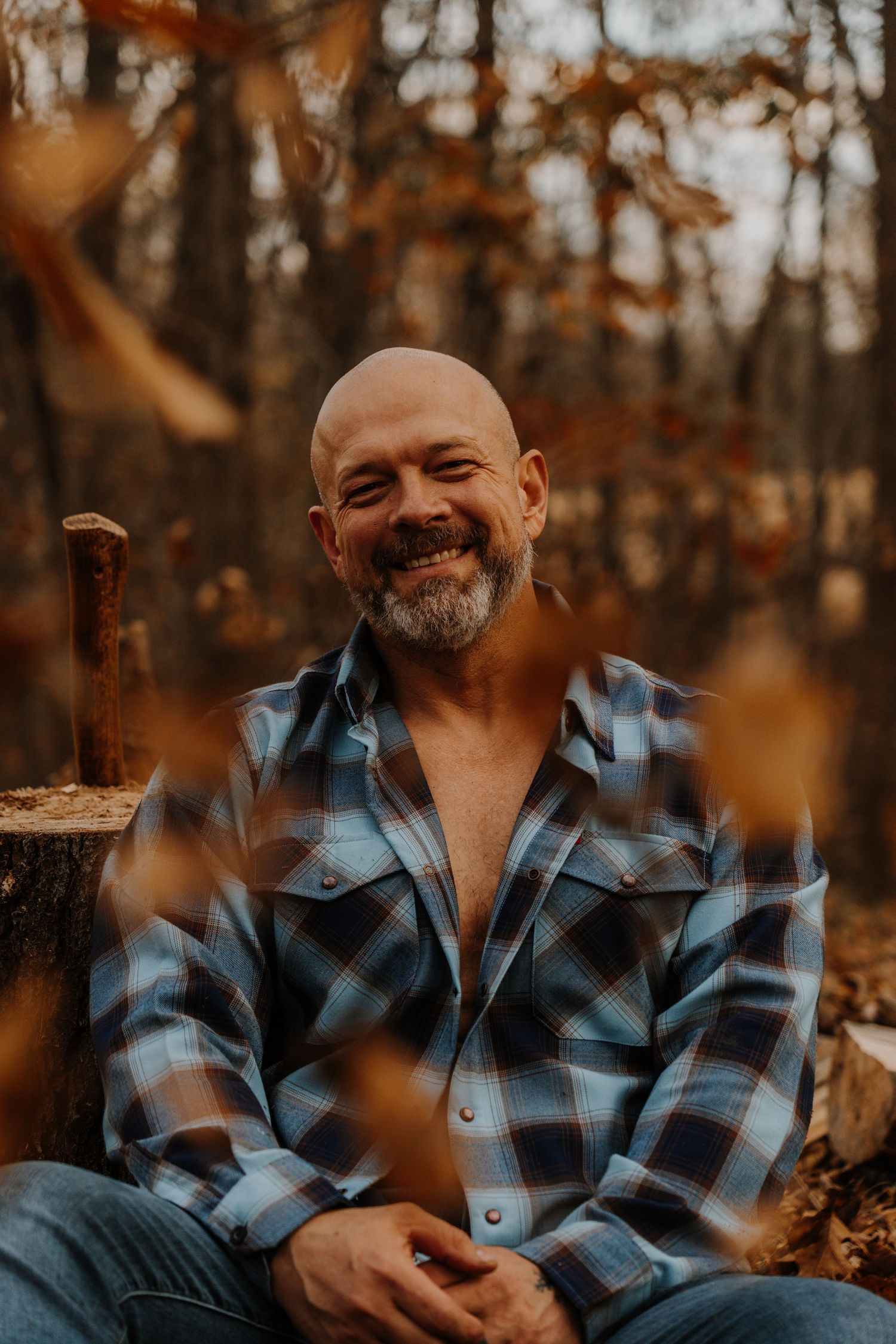 Person wearing blue plaid flannel shirt poses outdoors during autumn with warm lighting and fall foliage in background.