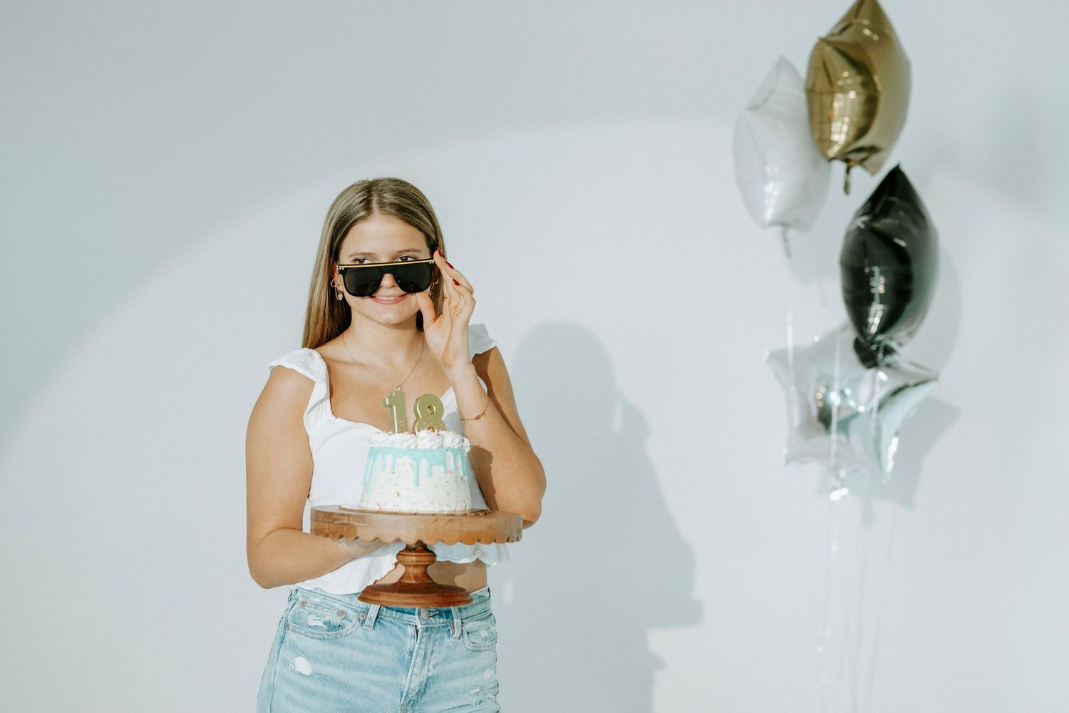 Person in sunglasses and light denim stands against white wall with decorative masks displayed.