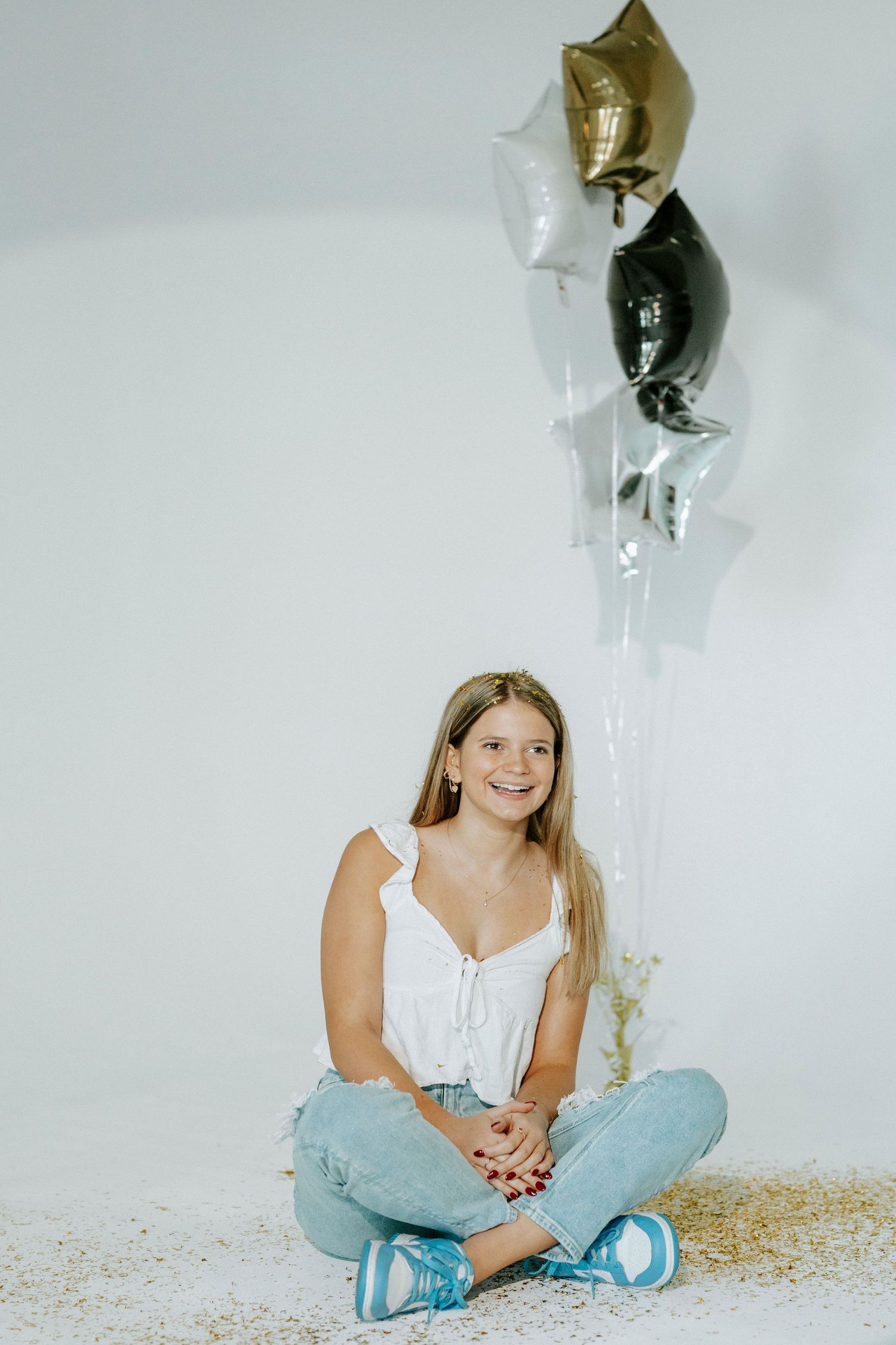 A person in light blue pants sits cross-legged on a white floor with black balloons floating above.