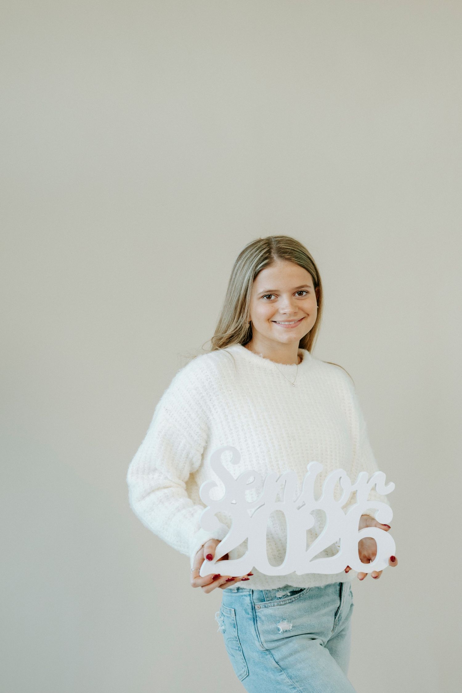 Person wearing a cozy white knit sweater and light blue jeans poses against a neutral background.