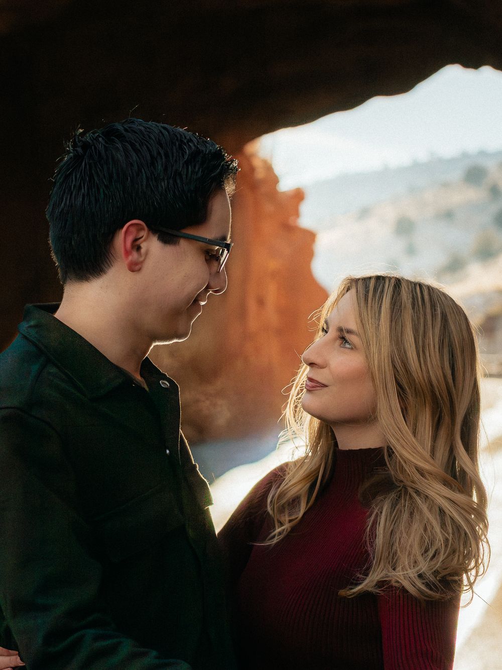 A romantic couple gazes at each other while backlit by warm sunlight during an outdoor portrait session.