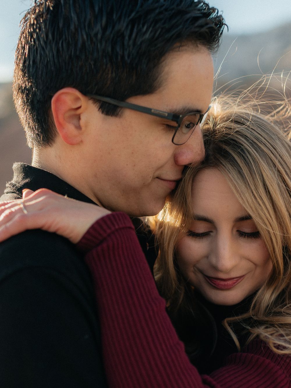 A tender romantic moment between a couple embracing at sunset, with soft golden light illuminating their faces.