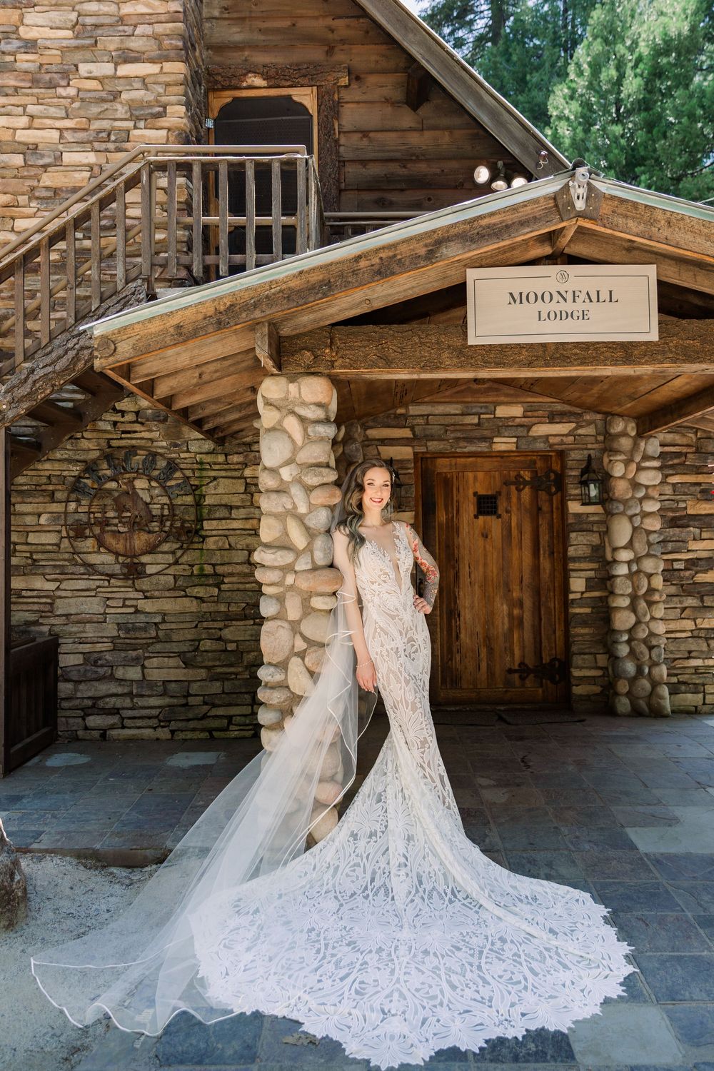 Stunning lace wedding dress with dramatic train photographed against rustic stone lodge exterior.