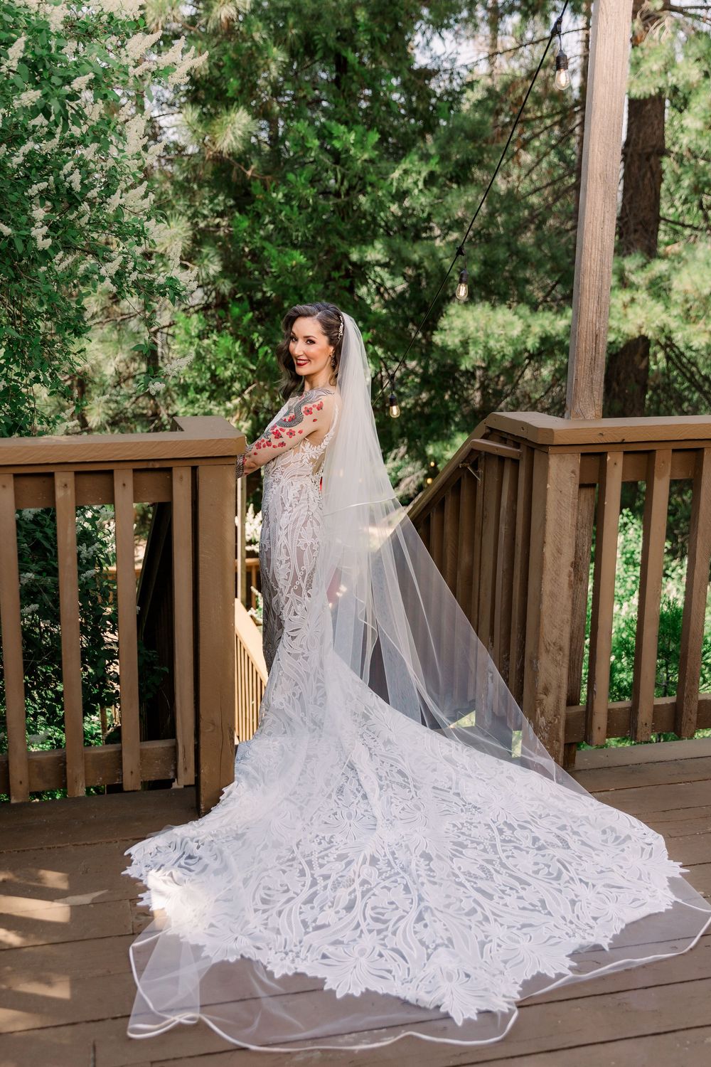 Elegant bridal portrait on wooden deck with flowing lace gown and cathedral veil.