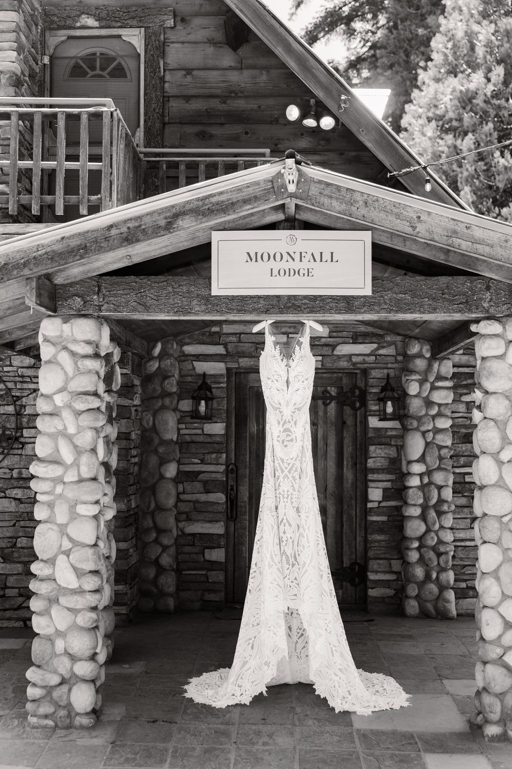 Elegant lace wedding dress hanging outside rustic log cabin lodge entrance.