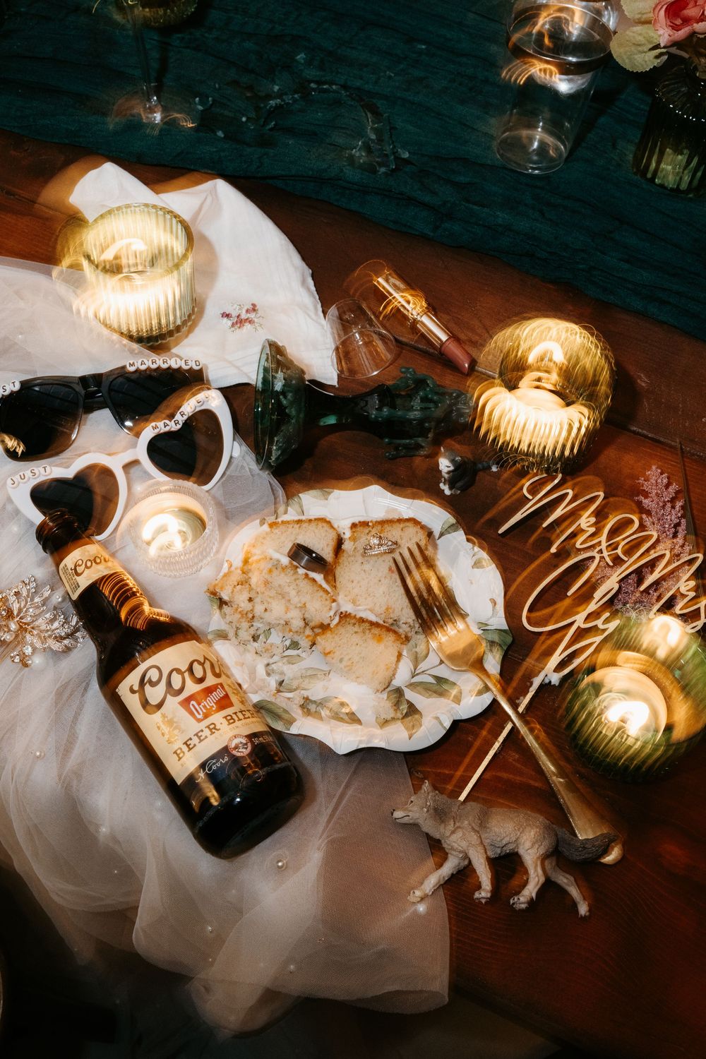 Empty beer bottles and glowing candles create a moody atmosphere on a dark wooden surface.