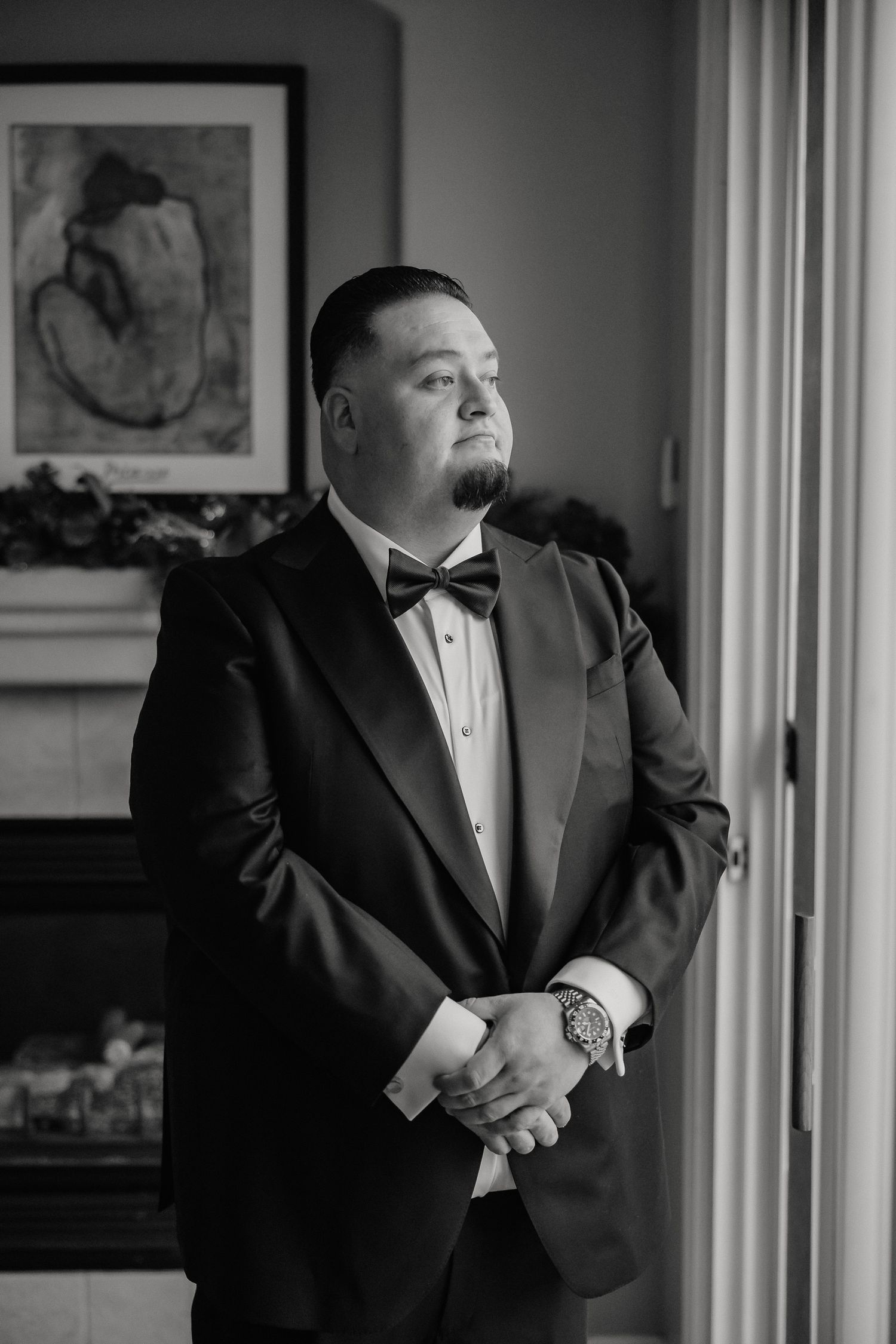 Black and white portrait of a person in formal attire standing by a window.