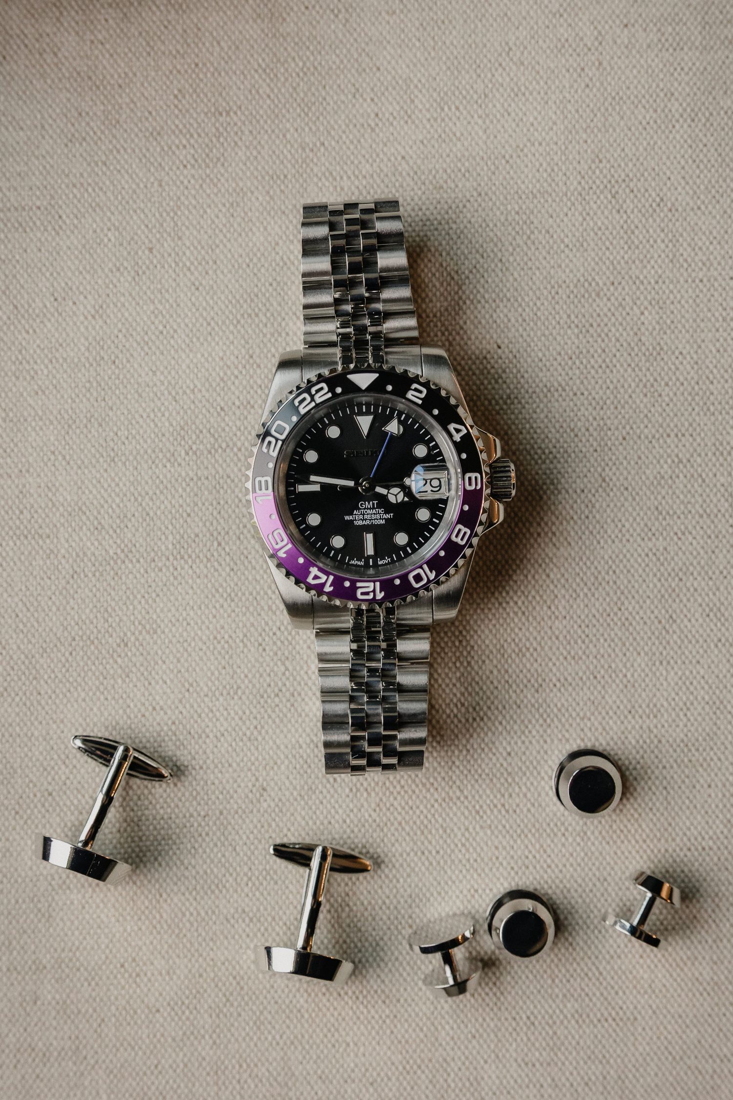 Close-up view of a black luxury watch and matching cufflinks arranged on a beige surface.