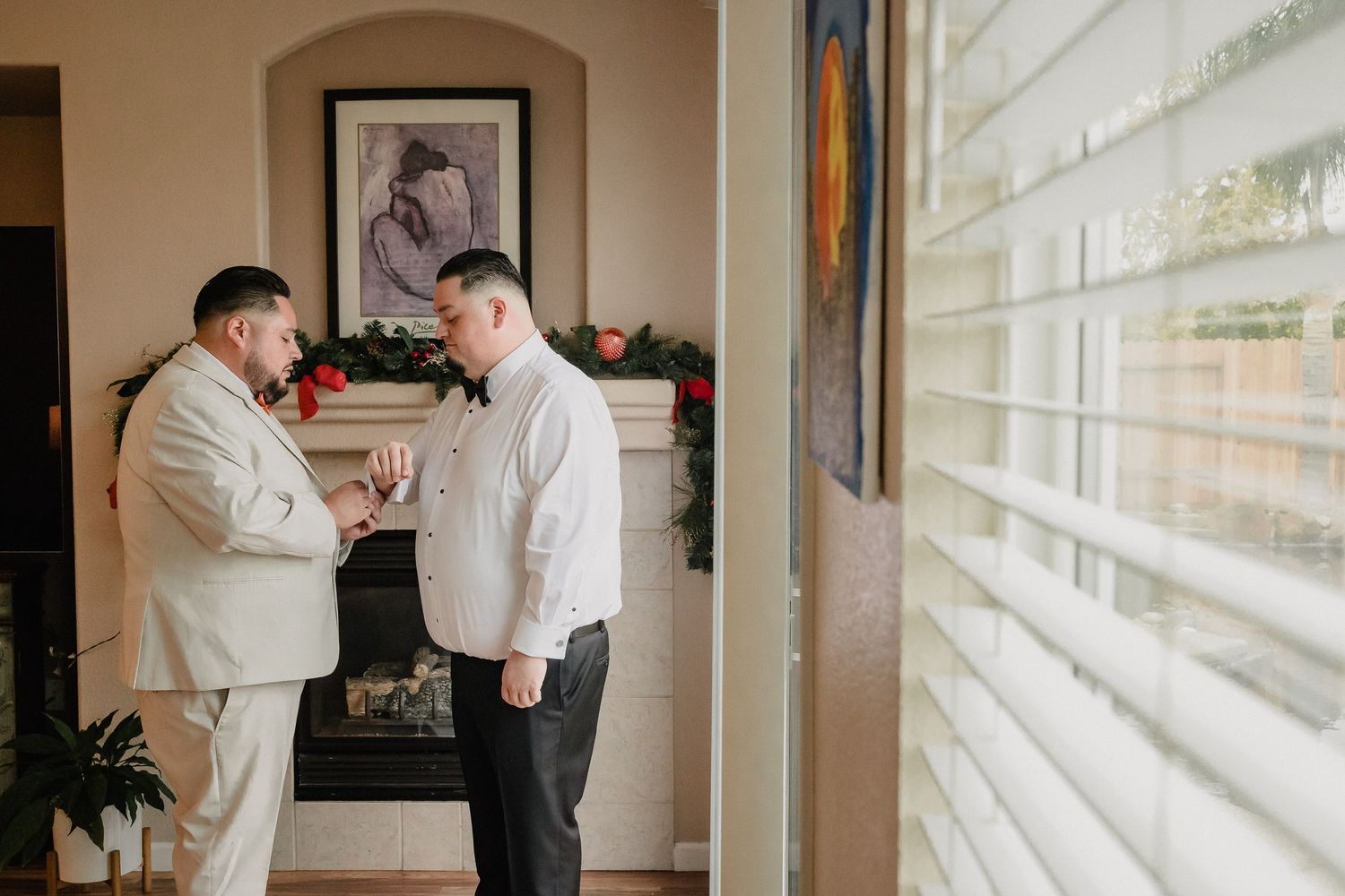Wedding preparation scene with formal attire being adjusted near bright windows in an indoor setting.