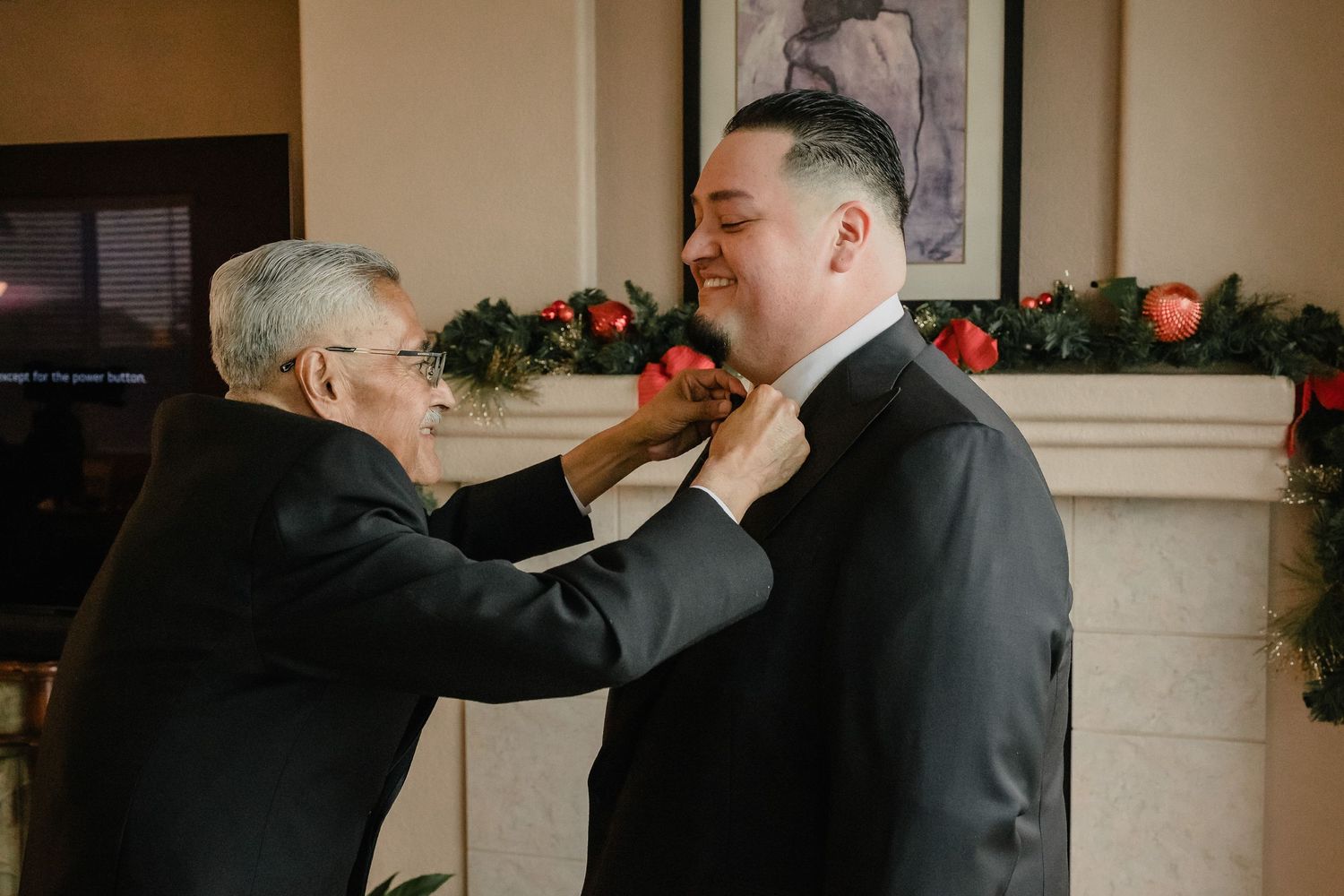 Two people helping with formal attire adjustments during wedding preparations.