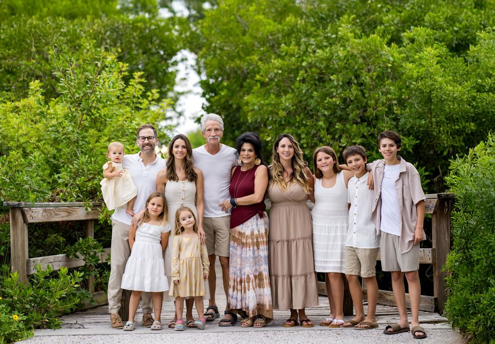 Wedding party members in coordinated white and beige attire pose together on a garden path.