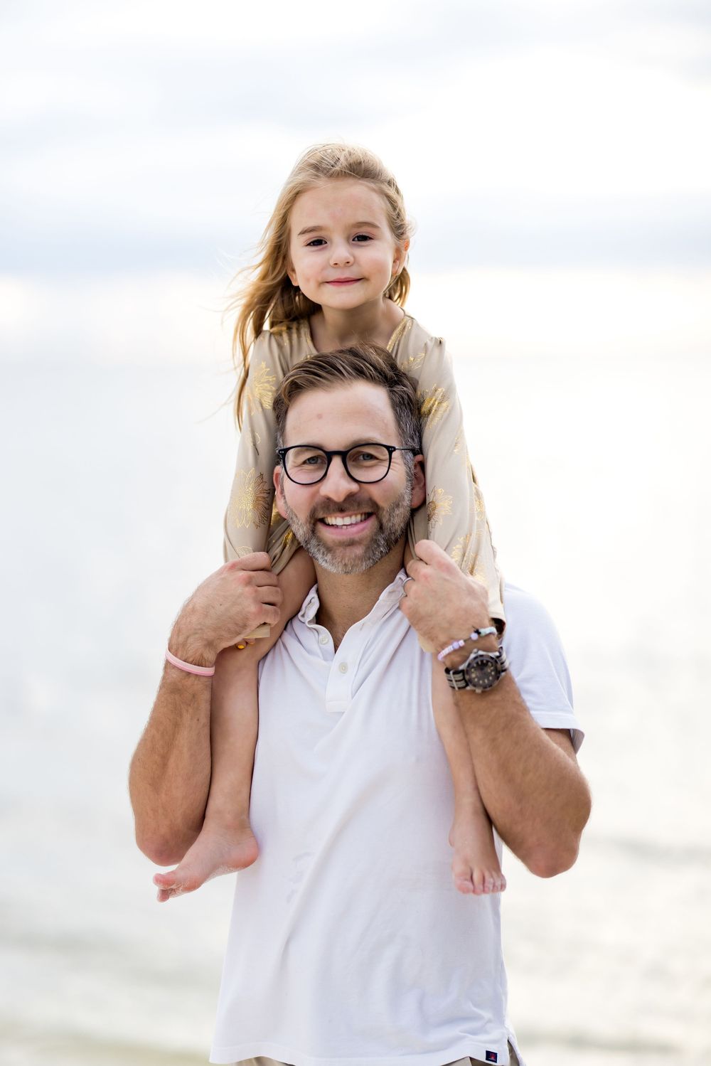 A parent and child share a joyful moment together at the beach with the child riding on shoulders.