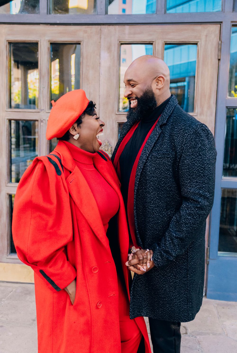 A couple shares a joyful moment together, with one wearing a vibrant red coat and beret and the other in a dark winter coat.