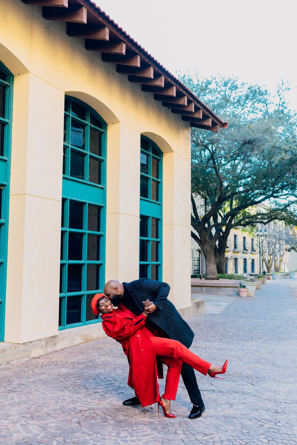 Two people in a dancing pose outside a Spanish colonial style building with turquoise windows and yellow walls.