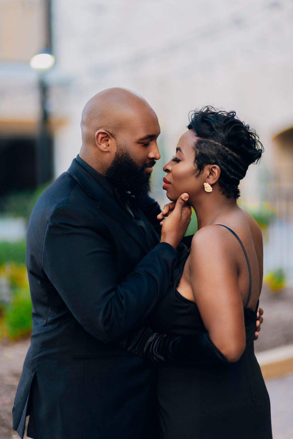 A loving couple in formal black attire share an intimate moment together outdoors.