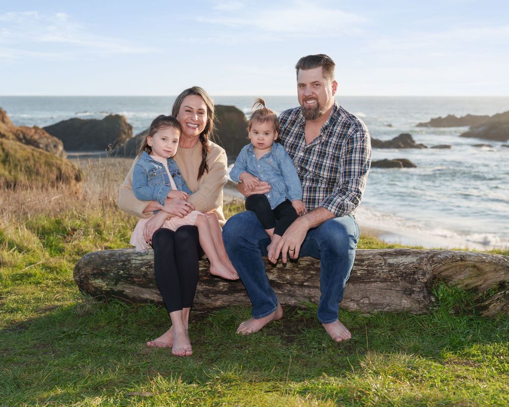 A family sits together on coastal rocks during sunset at a scenic beach with crashing waves and rugged shoreline.