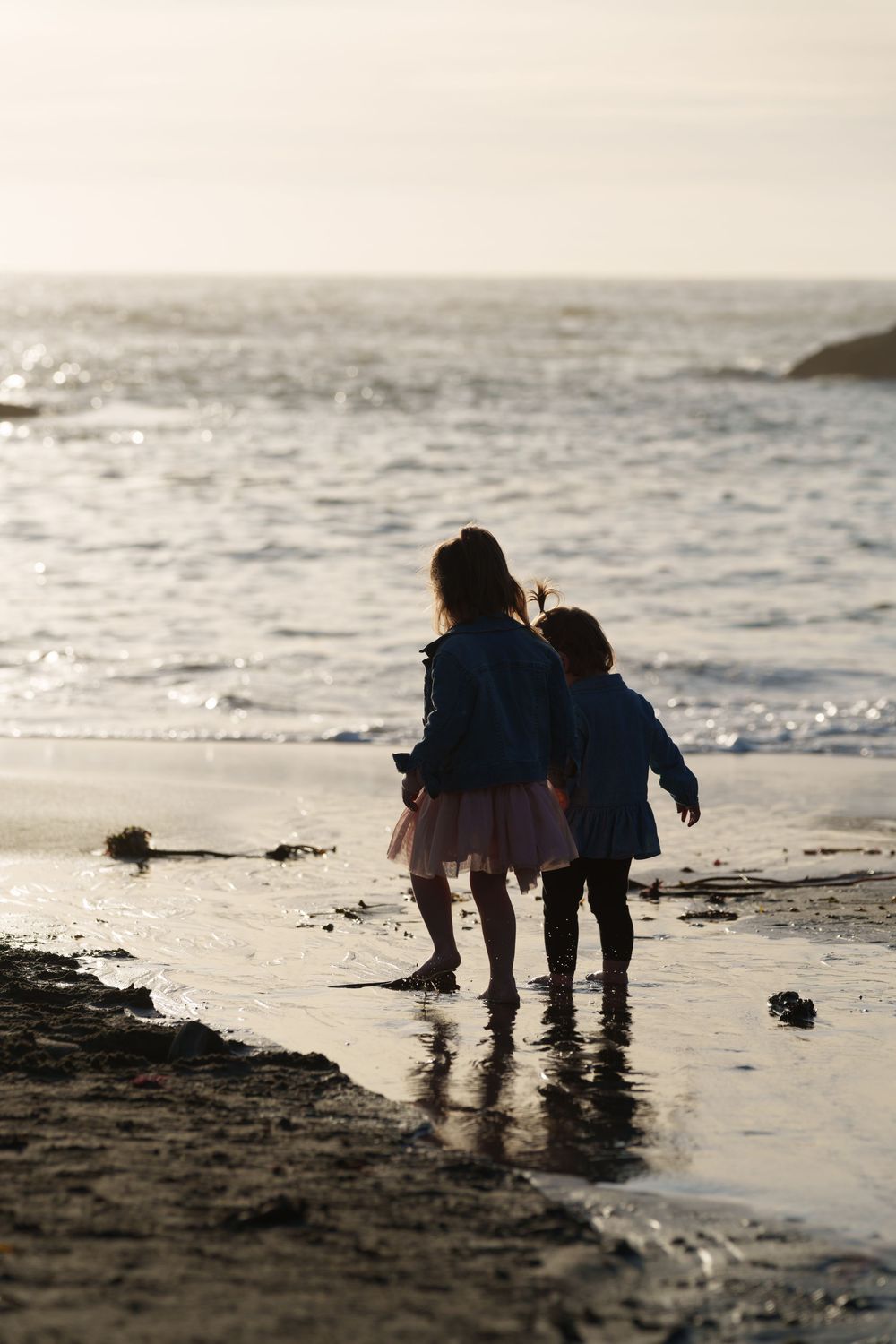 Silhouetted figures explore the shoreline together at sunset as gentle waves lap at the beach.