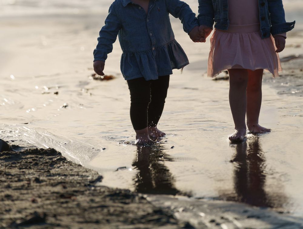 Close-up view of feet walking along wet sandy beach shore at sunset.