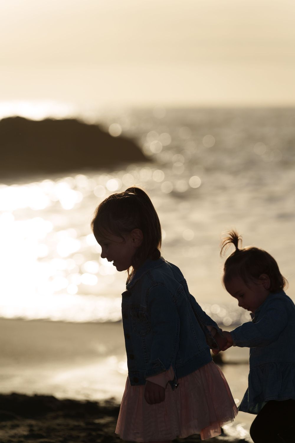 Silhouetted figures share tender moments against a golden sunset over the ocean.