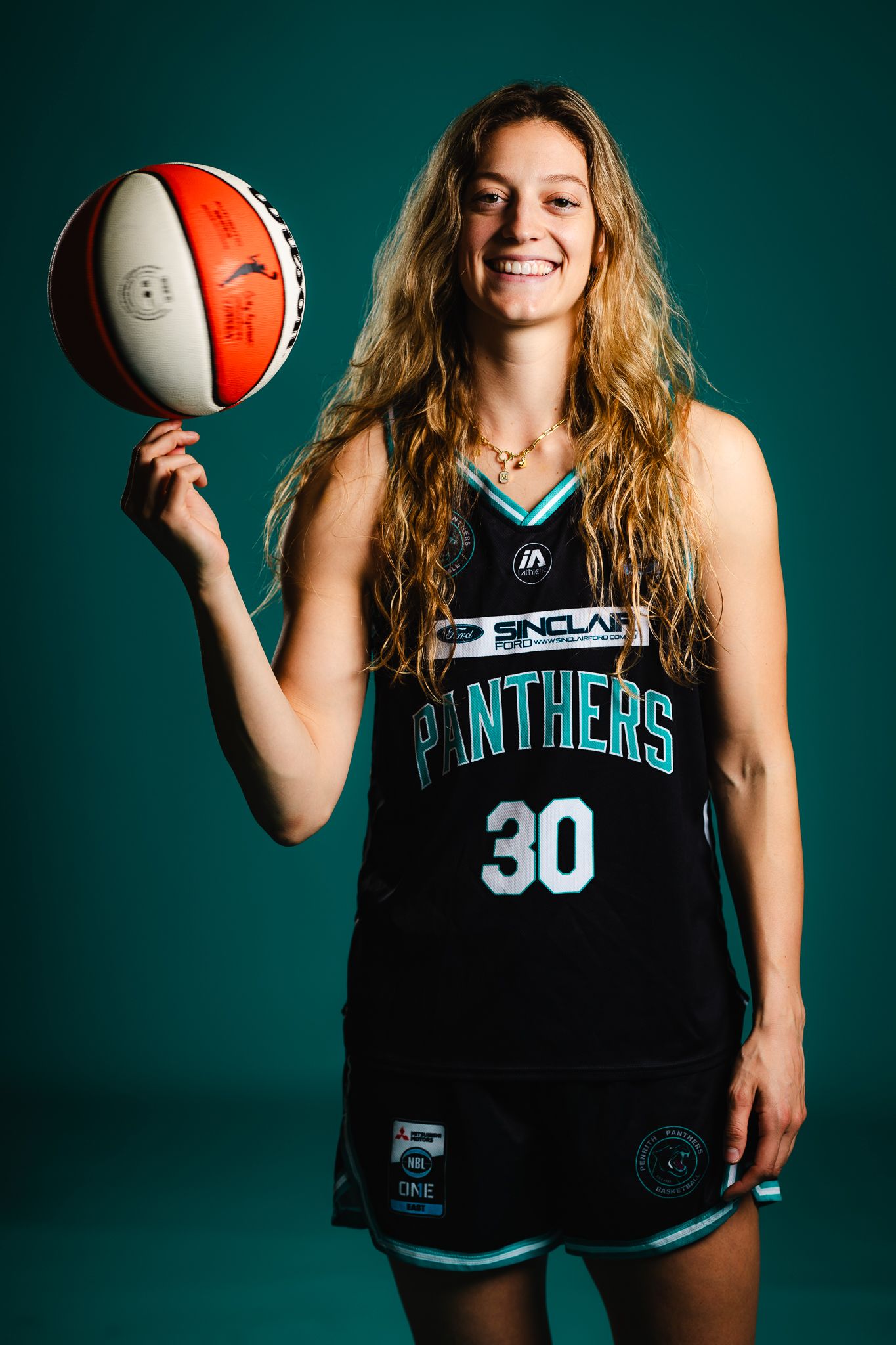 Basketball player in Panthers jersey number 30 poses with ball against teal background in professional sports photo shoot.