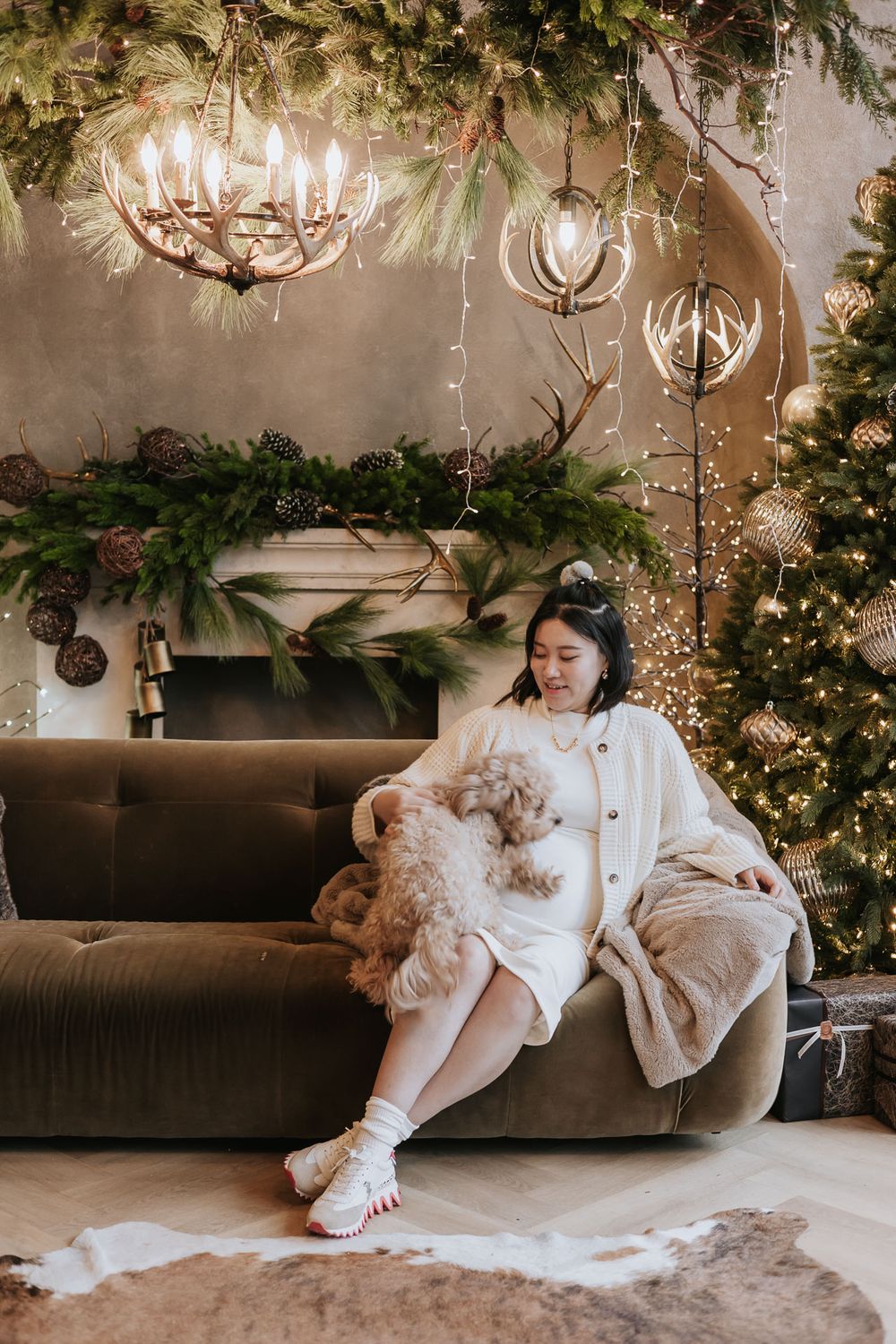 A cozy holiday scene with a brown couch, Christmas tree, chandeliers and festive greenery decorations.